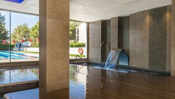 Un área de piscina interior moderna con caída de agua, ventanas amplias y vistas al exterior.