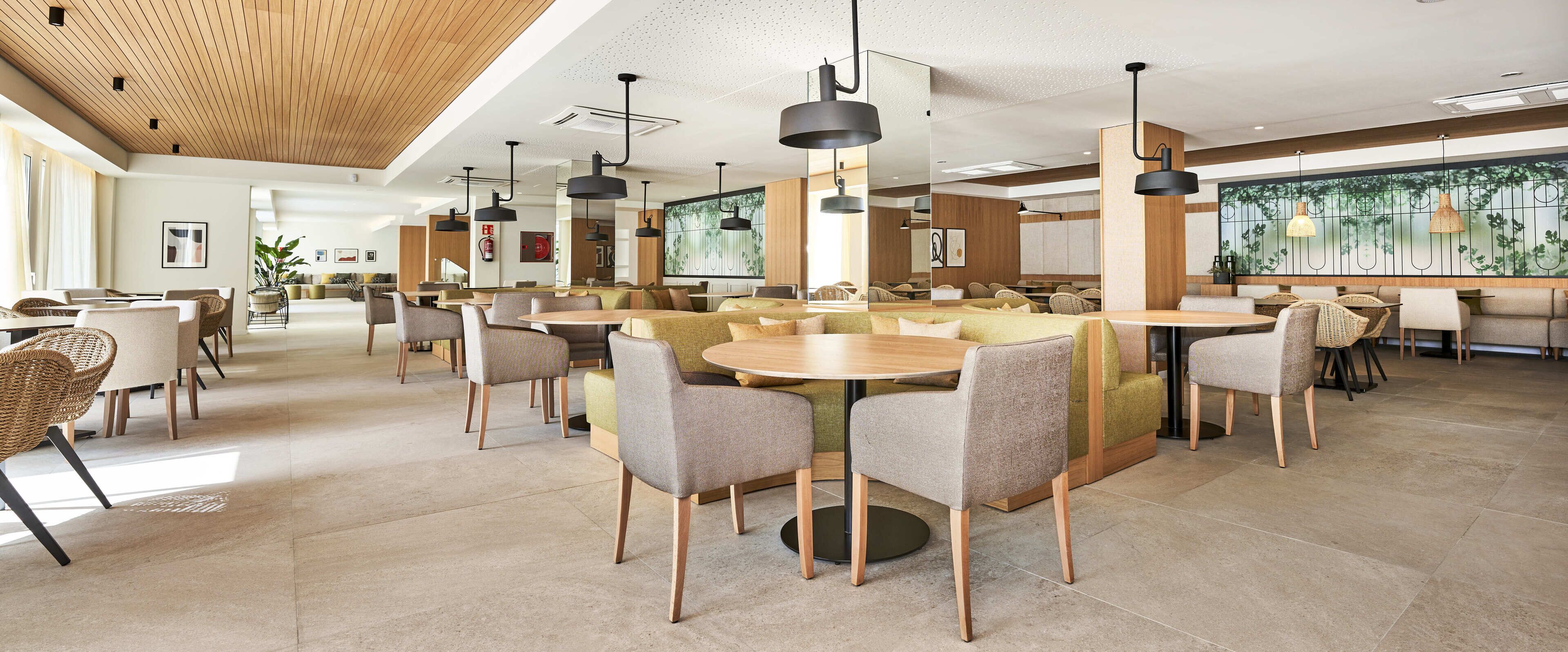 A spacious restaurant with round tables and chairs, wooden ceiling, and large windows.