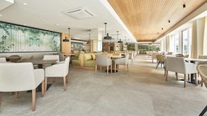 A modern restaurant interior with high ceilings, a large mural, and a variety of seating options including tables and booths. - Hoposa Hotel & Apartments Villaconcha (Pollenca)