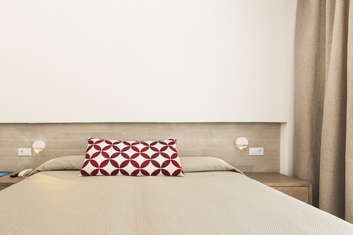 A neatly arranged hotel room with a bed, a chair, a nightstand, and a bedside table.