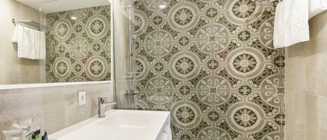 A modern bathroom with a large white sink, a glass shower enclosure, and patterned tiles.