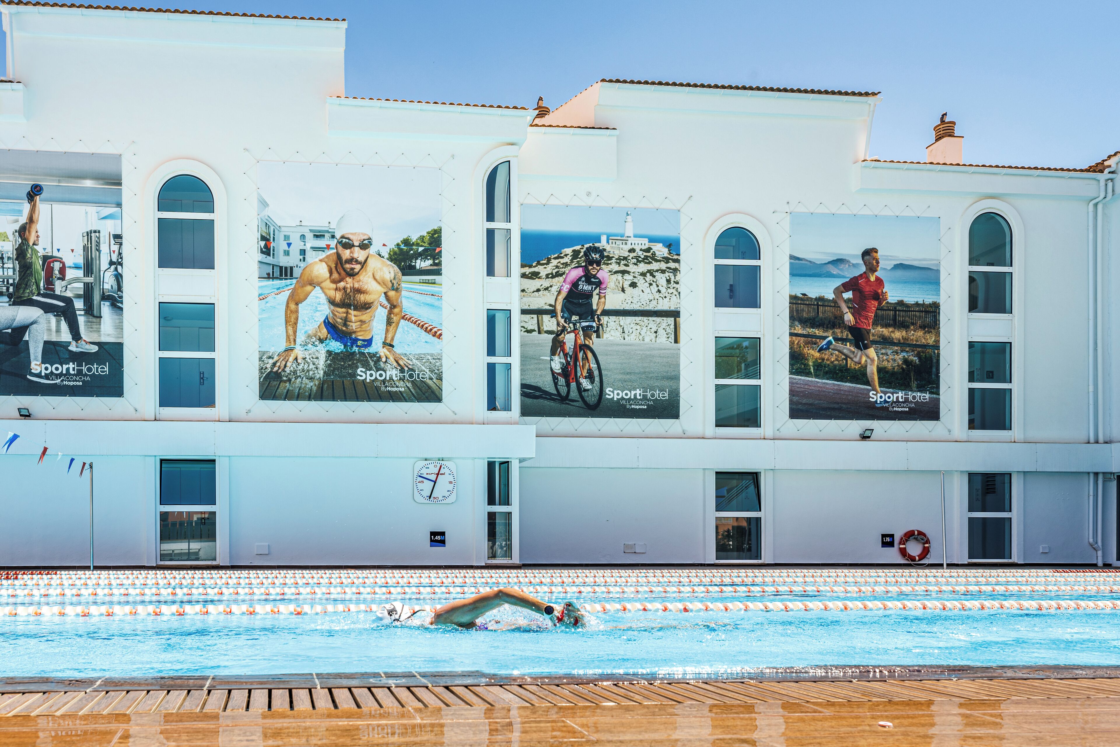 A building with a swimming pool, large windows, and advertisements for Sport Hotel.