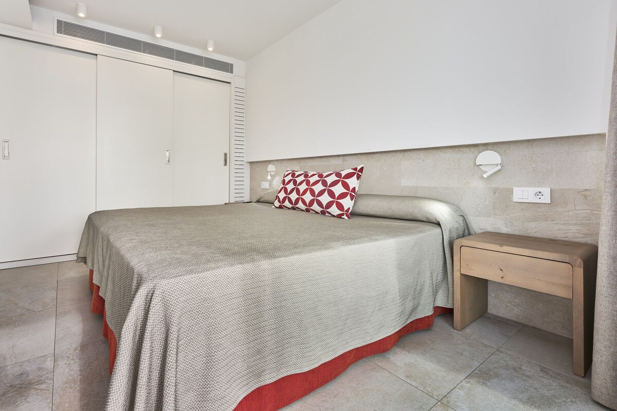 A bedroom with a bed, a nightstand, a wardrobe, and a wall-mounted light.