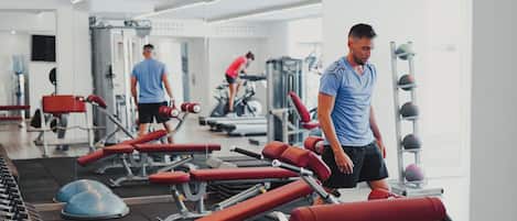 Gimnasio con equipo de ejercicio, una persona caminando y otra entrenando.