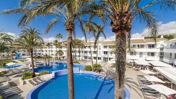A resort with a central swimming pool, multiple palm trees, and a building with balconies.