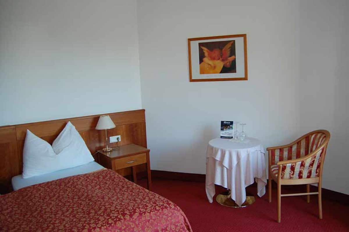 A hotel room with a bed, a nightstand, a table with a chair, and a framed picture on the wall.