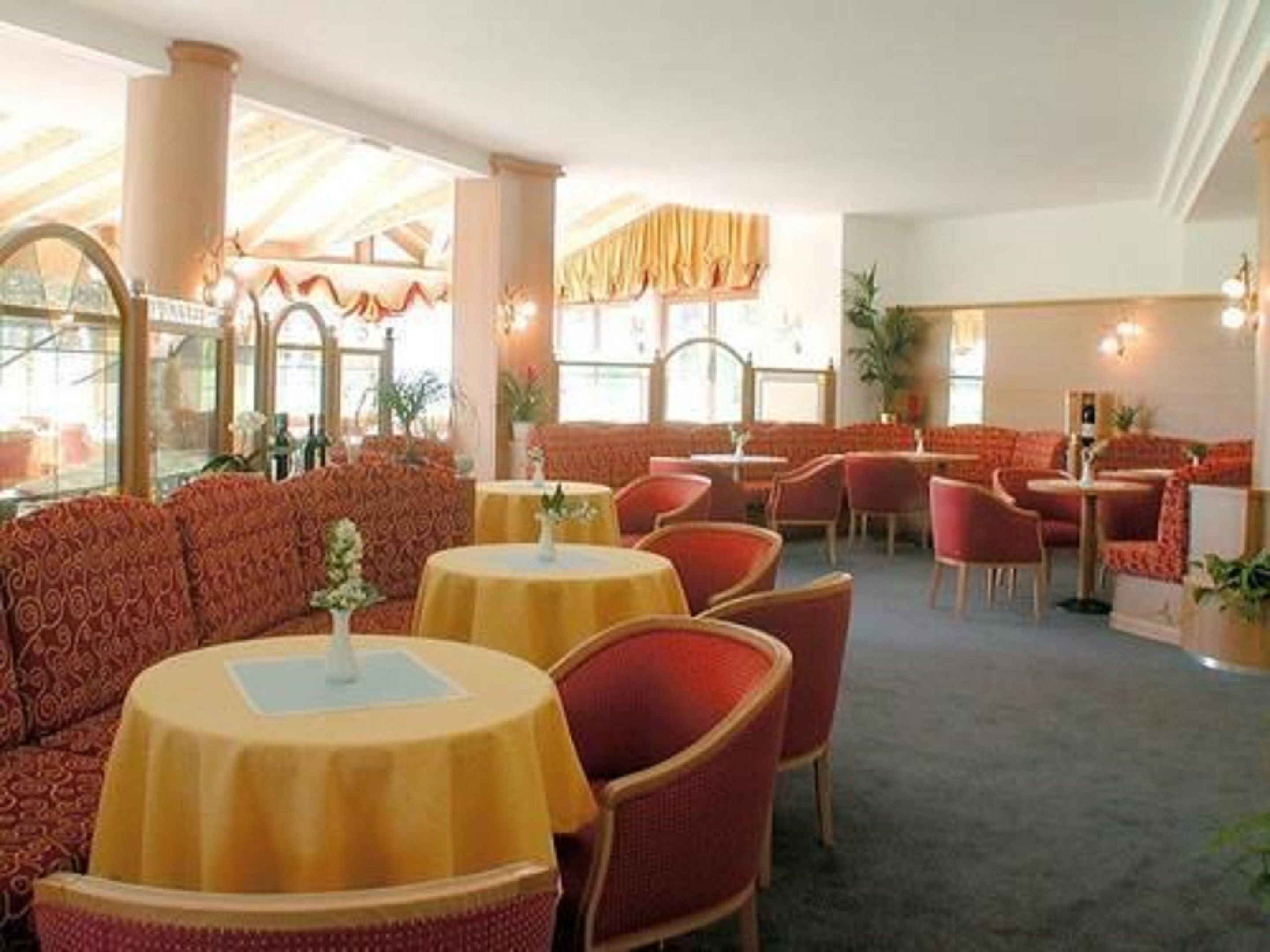 A restaurant with red upholstered seating, yellow tablecloths, and a classic interior design.