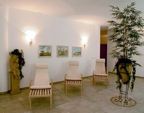 Ein Zimmer mit drei Holzstühlen, einer großen Topfpflanze und drei gerahmten Bildern an der Wand.