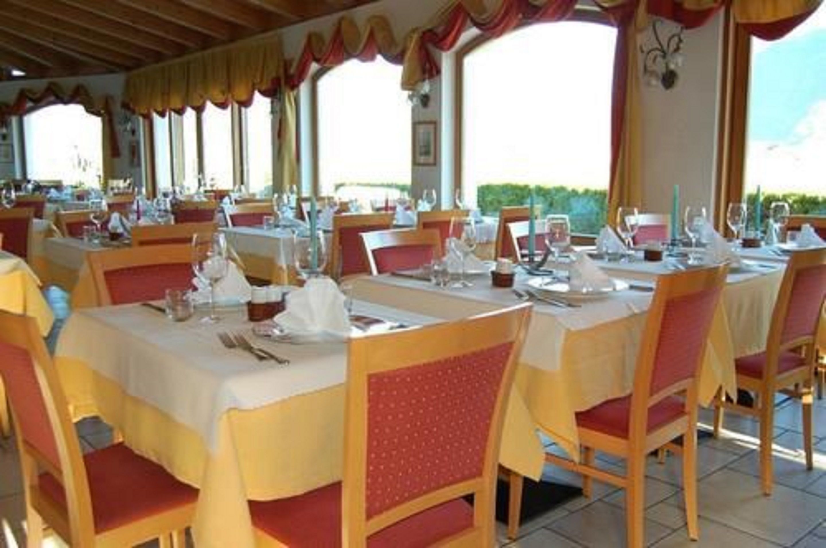 Un restaurant avec de nombreuses tables dressées pour le service, doté de chaises à revêtement rouge et de nappes blanches.