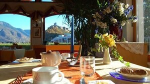 A dining table set with plates, cutlery, and a vase of flowers, with a mountain view in the background.