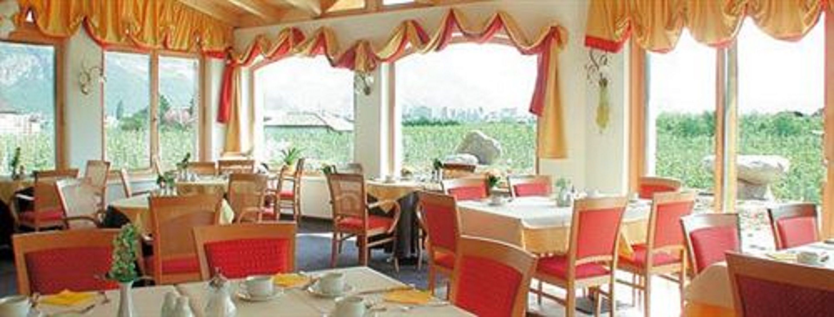 Un restaurant doté de nombreuses tables et chaises, de grandes fenêtres avec des rideaux et offrant une vue sur la verdure environnante.