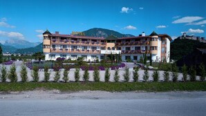 A hotel with multiple balconies, a mountain backdrop, and a castle-like structure nearby.