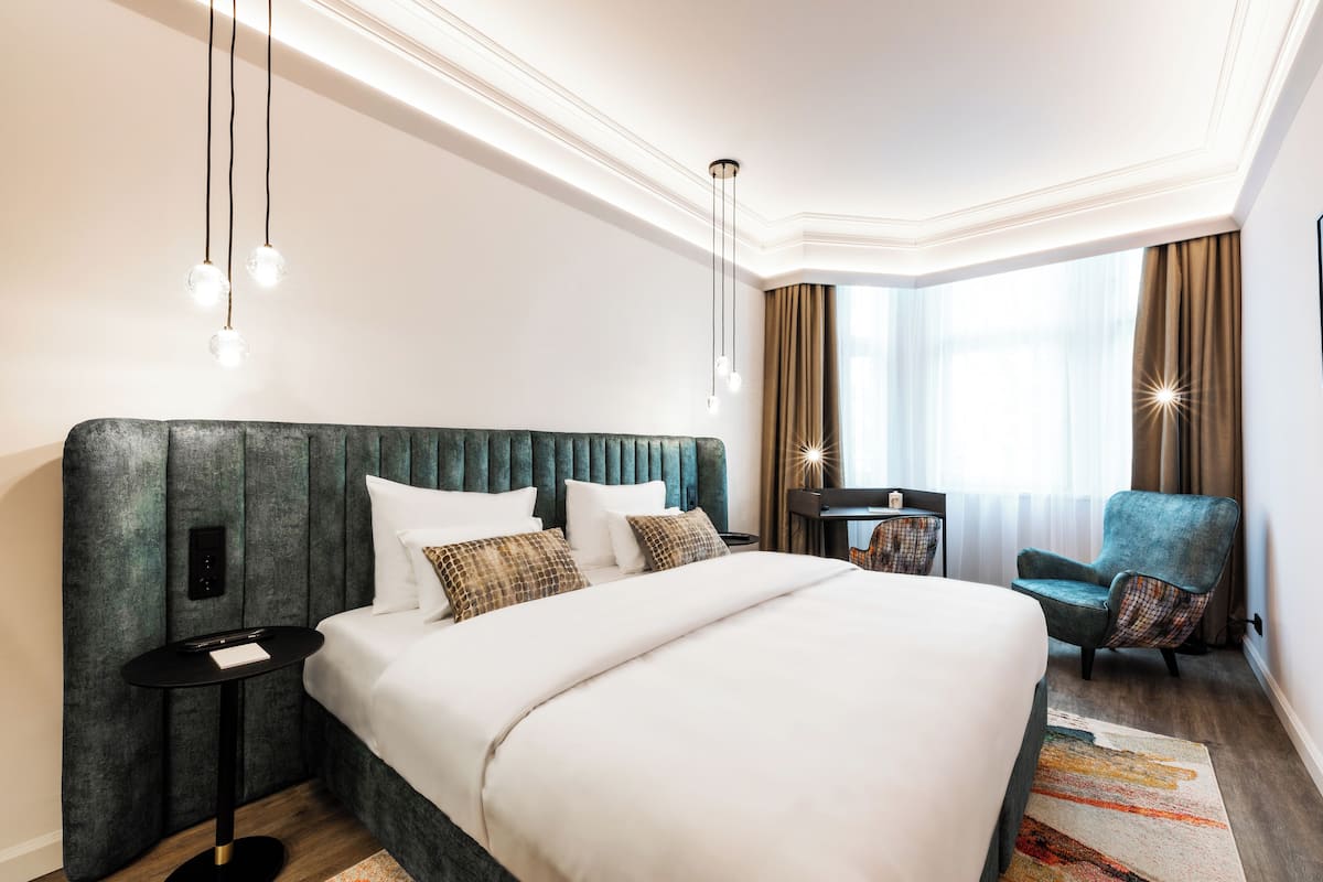 A hotel room with a large bed, a desk, a chair, and a window with curtains.