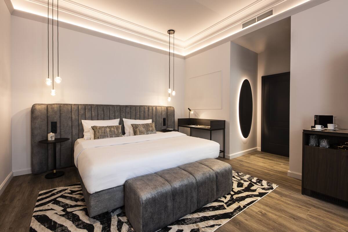 A modern bedroom with a large bed, bedside tables, a bench, and a desk with a chair.