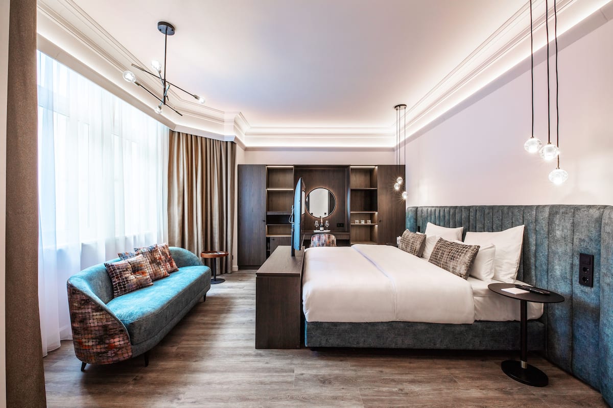 A modern hotel room with a large bed, a sofa, a desk, and a mirror.