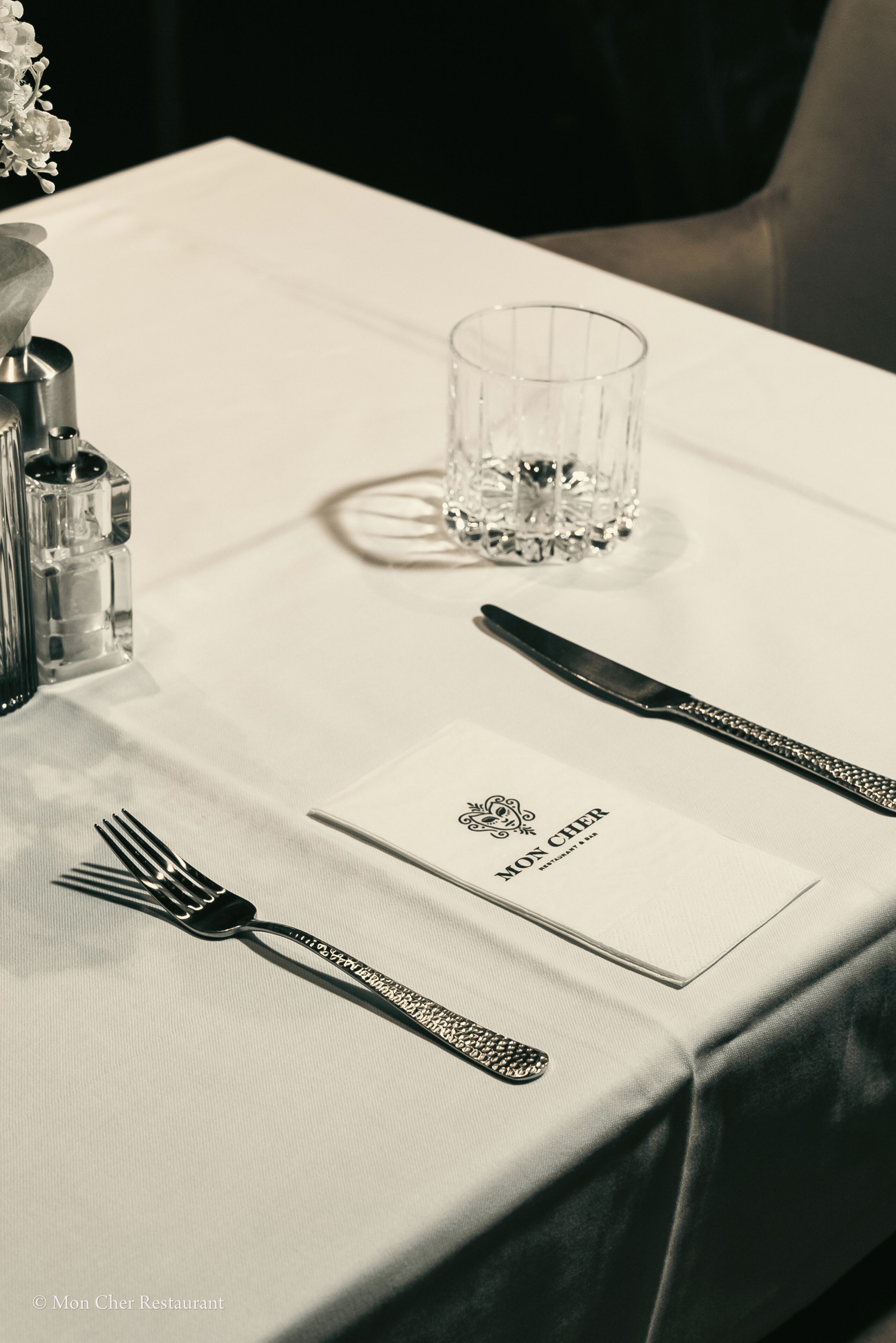 Una mesa de comedor dispuesta con cuidado, un menú, cubiertos y un vaso de agua.