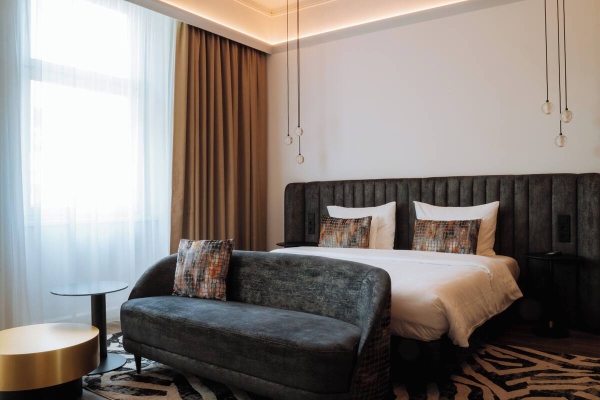 A modern hotel room with a large bed, a dark sofa, a small round table, and a zebra-patterned rug.