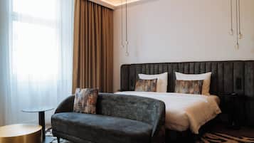 Una habitación de hotel moderna con una cama grande, un sofá oscuro, una mesita redonda y una alfombra con estampado de cebra.