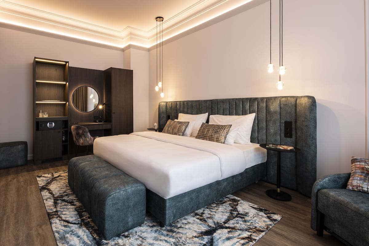 A modern bedroom with a large bed, a built-in wardrobe, a round mirror, and a bedside table.