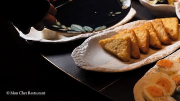 En buffet med forskellige retter, blandt andet et fad med skiveskåret brød, en skål med tomater og en skål med æg.