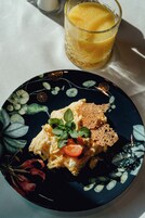 Um prato com ovos mexidos, fatias de tomate e um ramo de manjericão, acompanhado por um copo de suco de laranja.