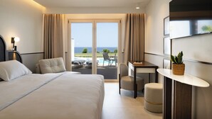 A hotel room with a bed, a desk, a chair, a small table, and a view of the sea through a glass door. - Iberostar Selection Creta Marine (Mylopotamos)