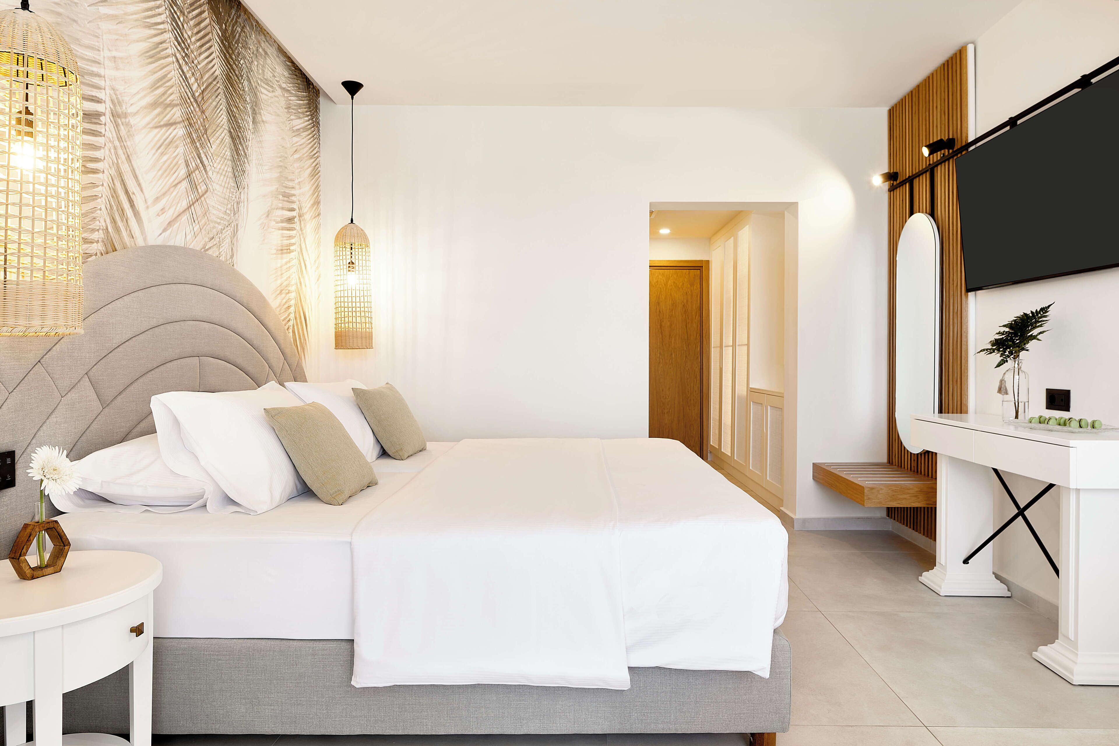 A modern bedroom with a large bed, bedside tables, a vanity with a mirror, and a television.