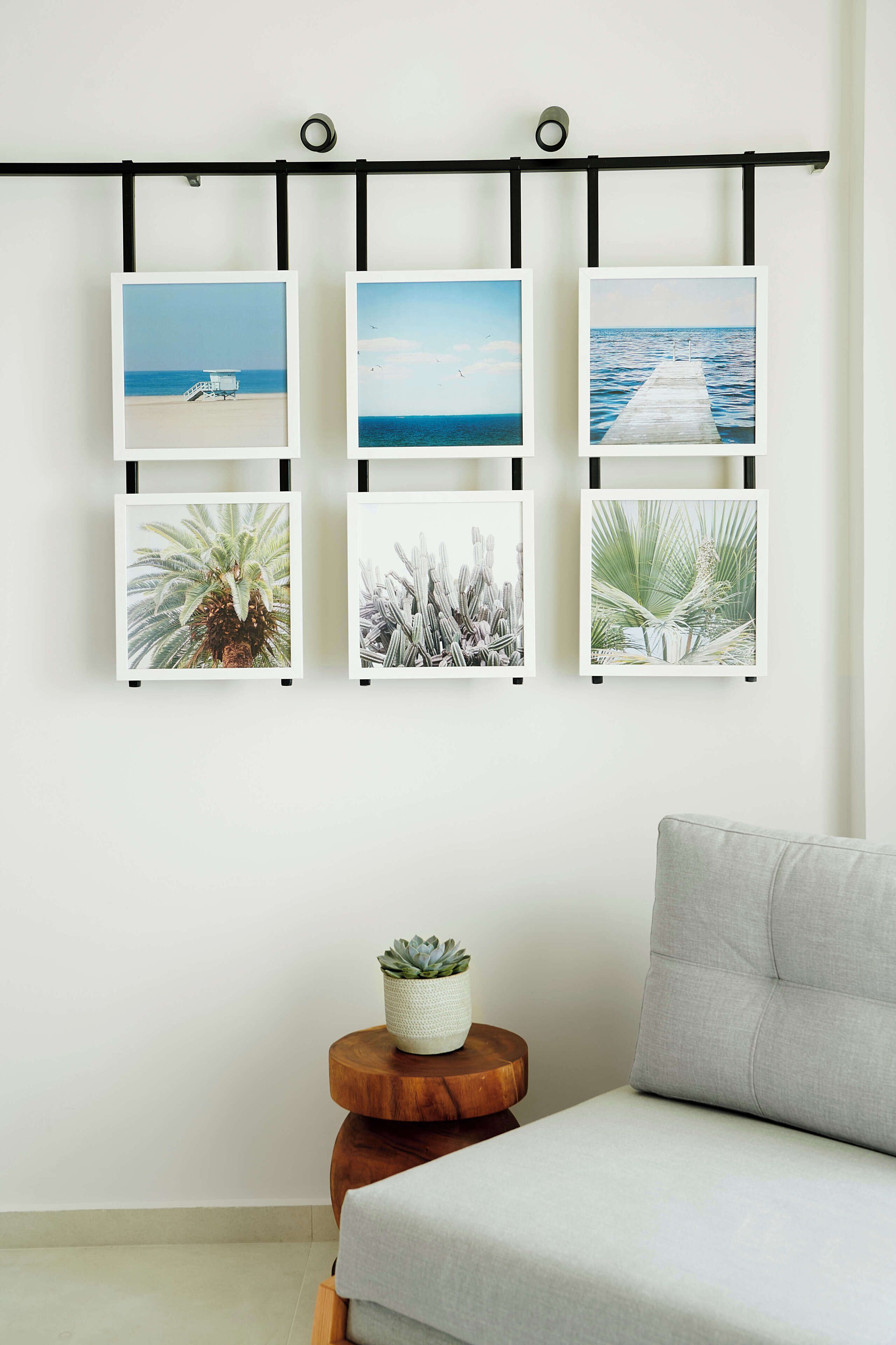 A wall with five framed pictures, a small round wooden table with a plant, and a grey sofa.