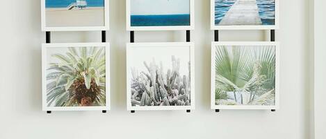 A wall with five framed pictures, a small round wooden table with a plant, and a grey sofa.