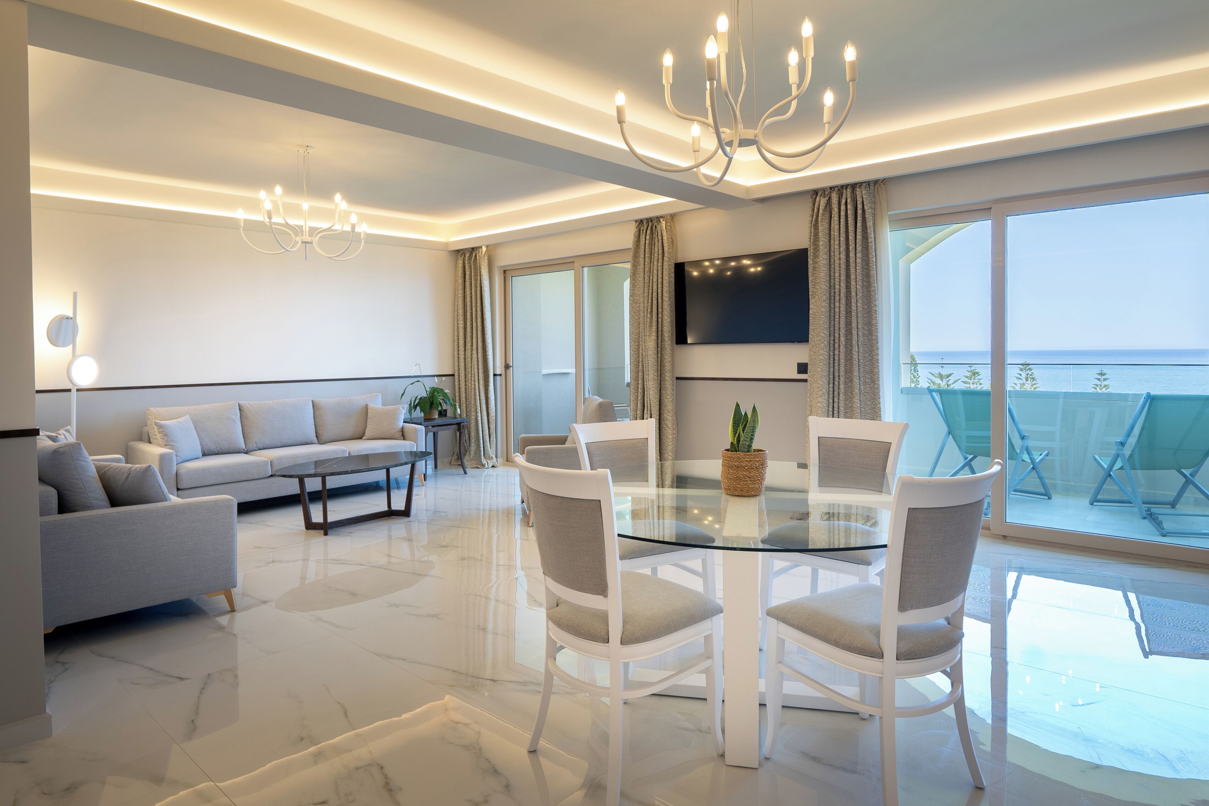 Una sala de estar moderna con una mesa de comedor de vidrio, sillas blancas, un sofá y una araña.