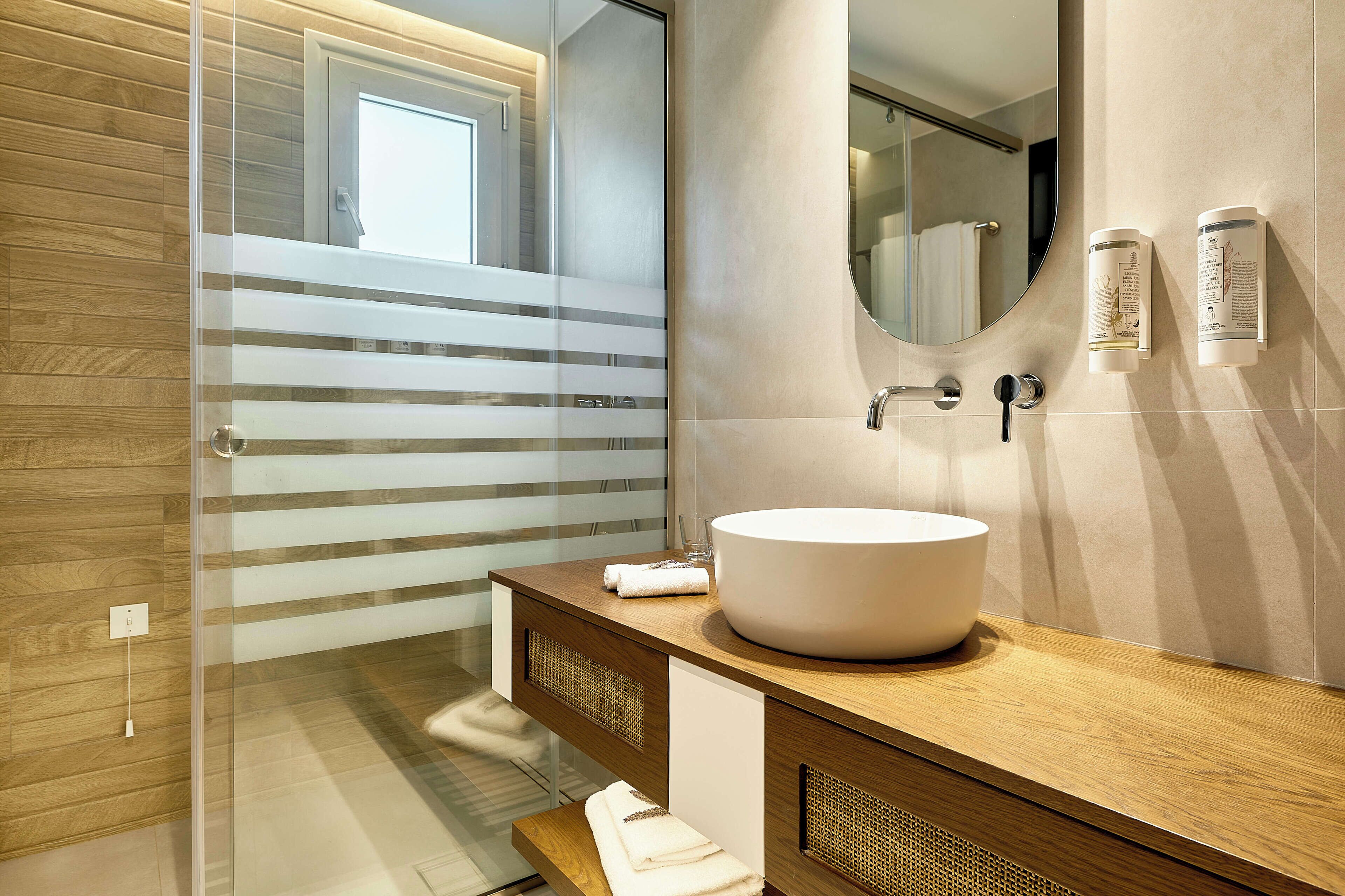 A modern bathroom with a large mirror, a round sink, and a glass shower enclosure.