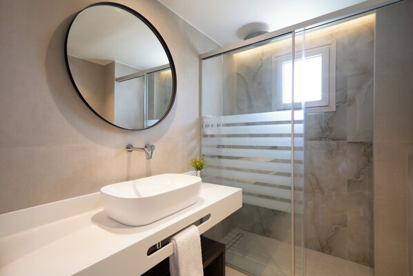 Un baño moderno con un espejo redondo, un lavabo blanco y un box de ducha de vidrio.