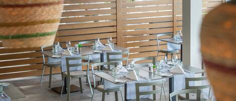 A restaurant with tables set for dining, hanging woven baskets, and a slatted wooden wall.