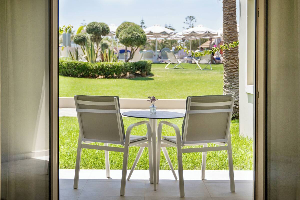 An outdoor seating area with two white chairs and a small round table, overlooking a well-maintained lawn and a distant view of a resort area.