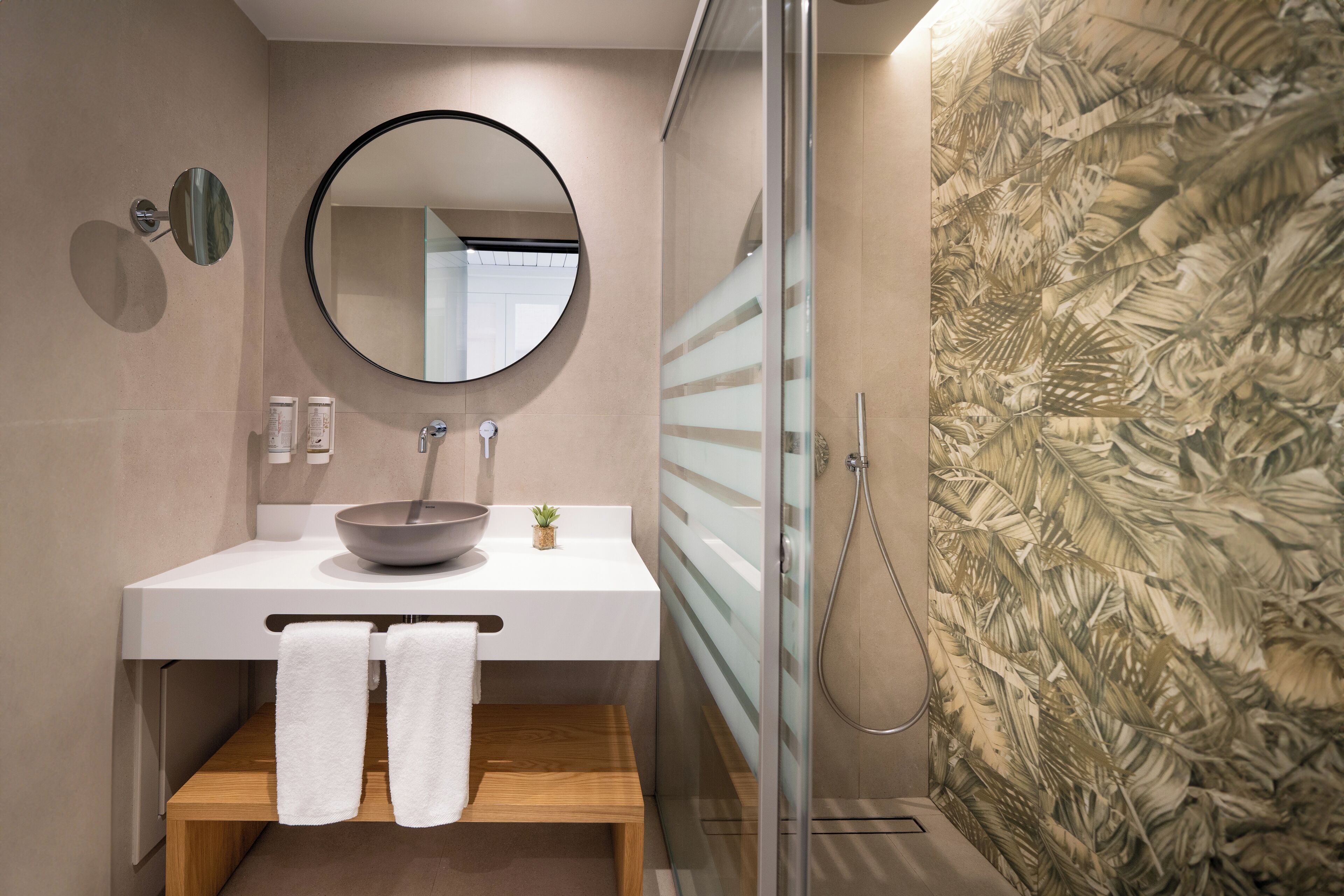 A modern bathroom with a round mirror, a bowl sink, and a glass shower enclosure.