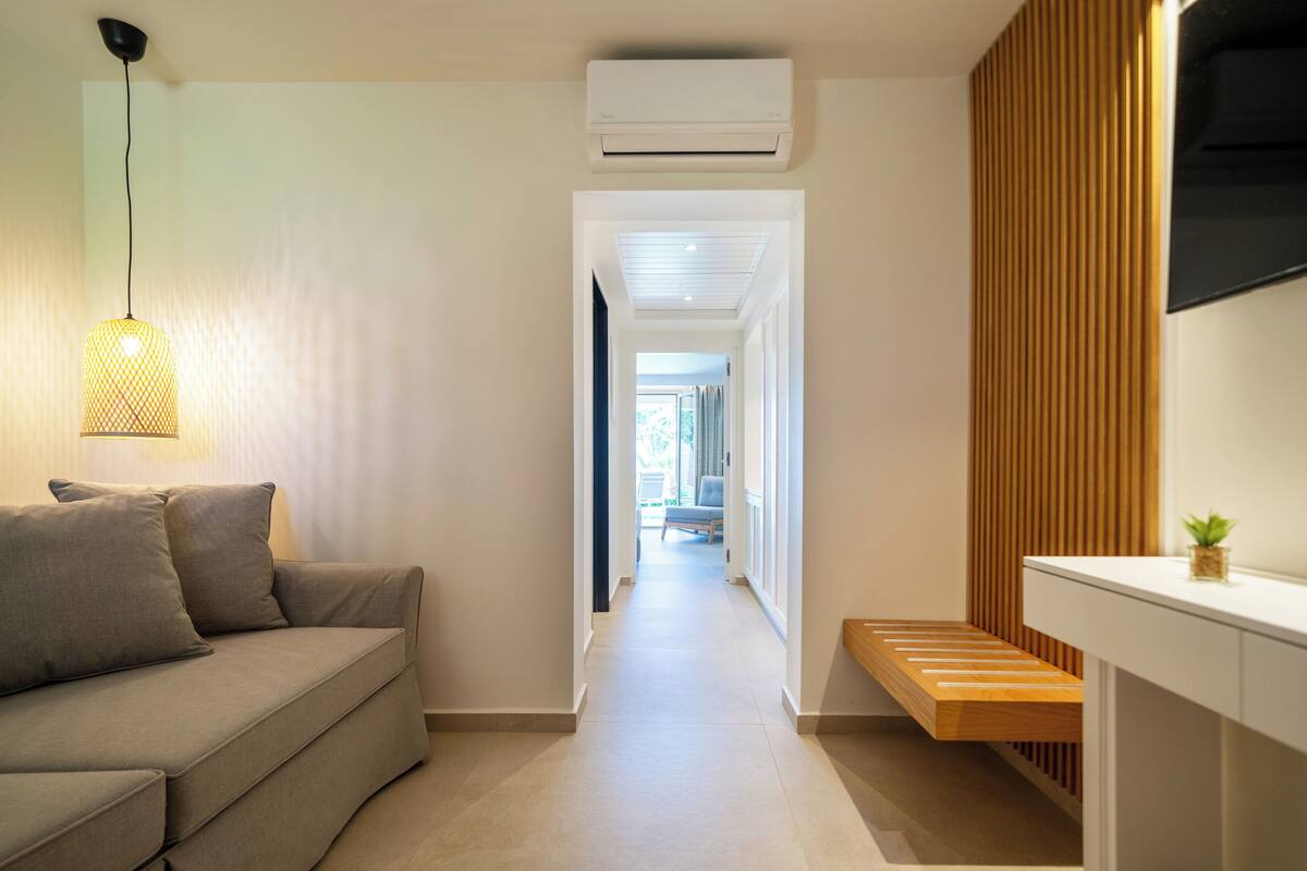 A hallway with a sofa, a hanging light fixture, a wooden bench, and a mounted TV.