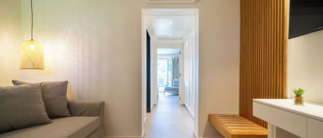 A hallway with a sofa, a hanging light fixture, a wooden bench, and a mounted TV.