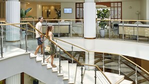 Un interior de varios niveles con techo de cristal, una escalera central y un área de descanso con vista al cielo.