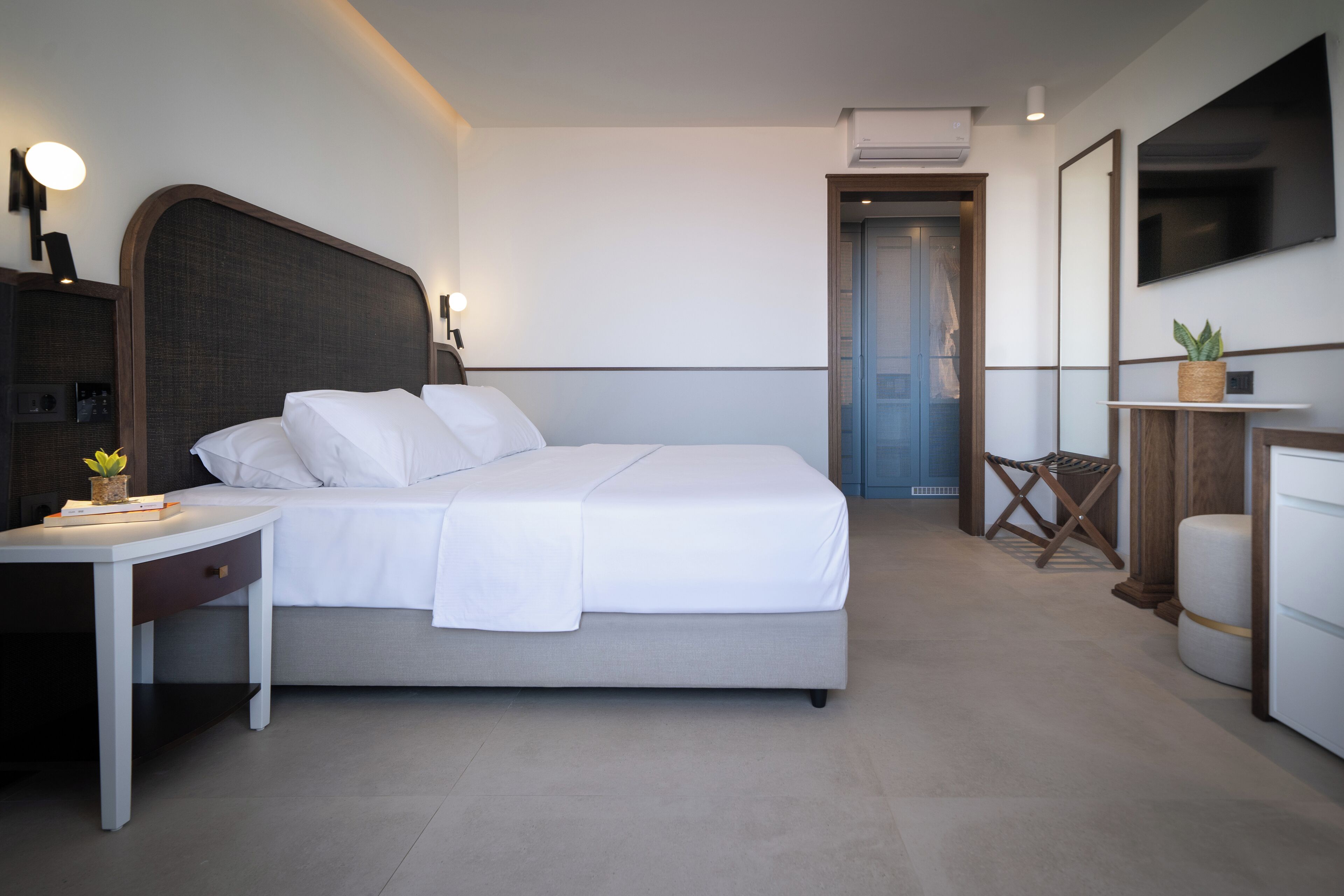 A modern hotel room with a large bed, bedside table, and a small desk with a lamp.