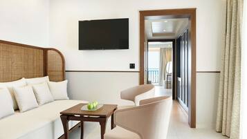 Habitación de hotel con sofá, una silla, una mesa con manzanas, un televisor de pantalla plana y vistas a través de un ventanal.