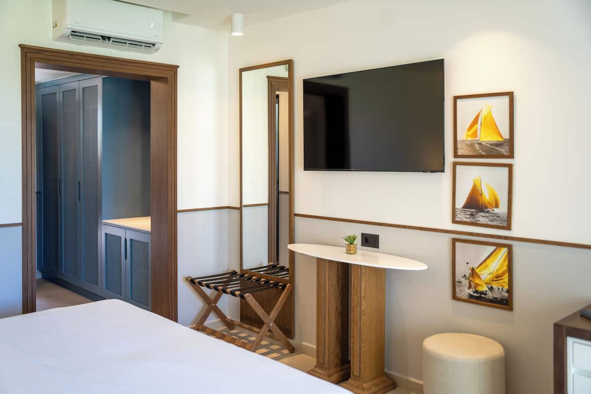 A hotel room with a bed, a TV mounted on the wall, a small round table with a plant, and a mirror.