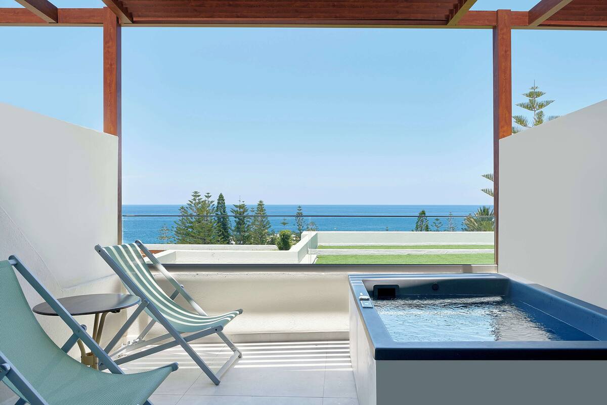 A balcony with two striped lounge chairs, a small table, and a hot tub.