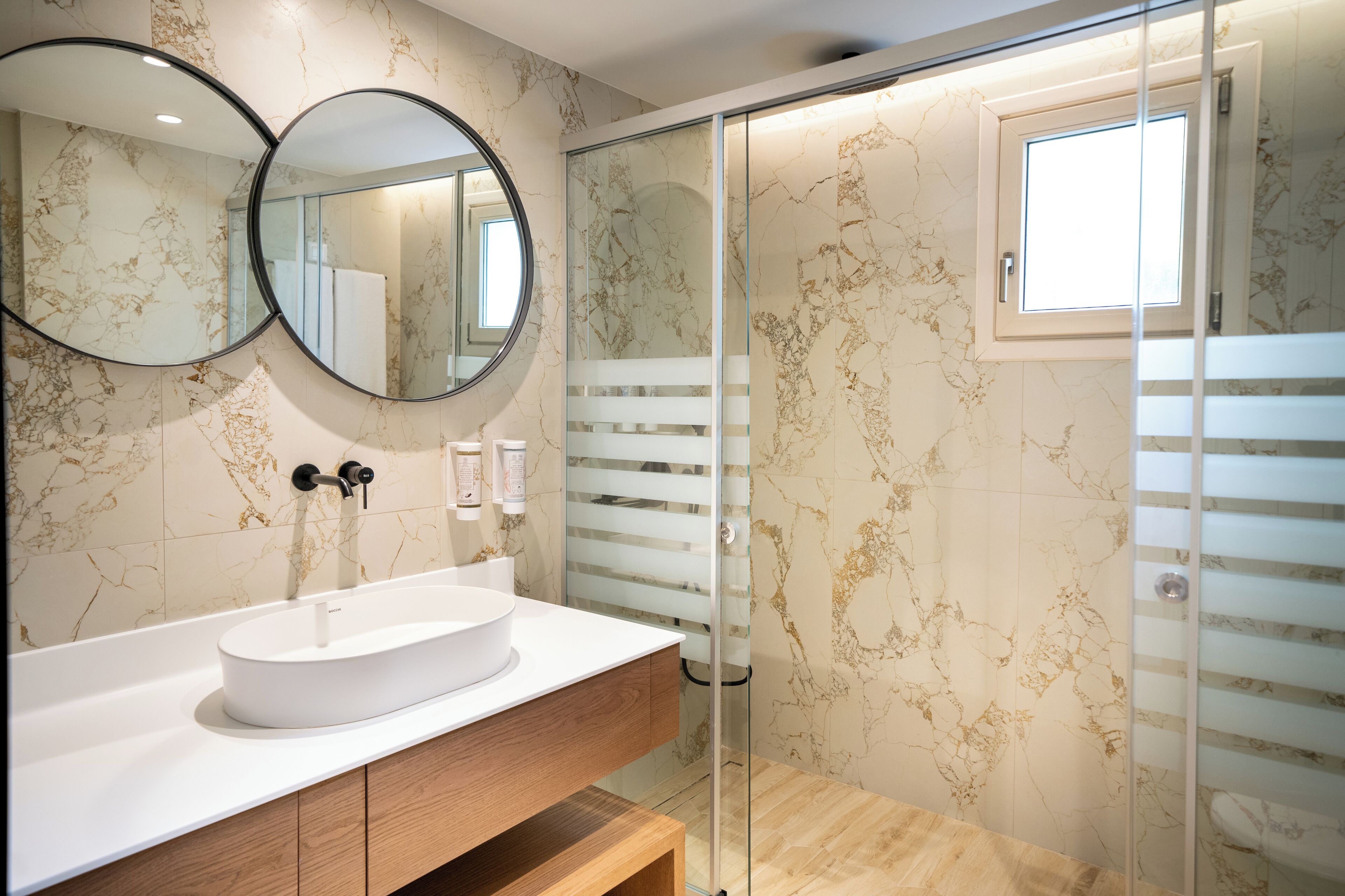 A modern bathroom with a white sink, two round mirrors, and a glass shower enclosure.