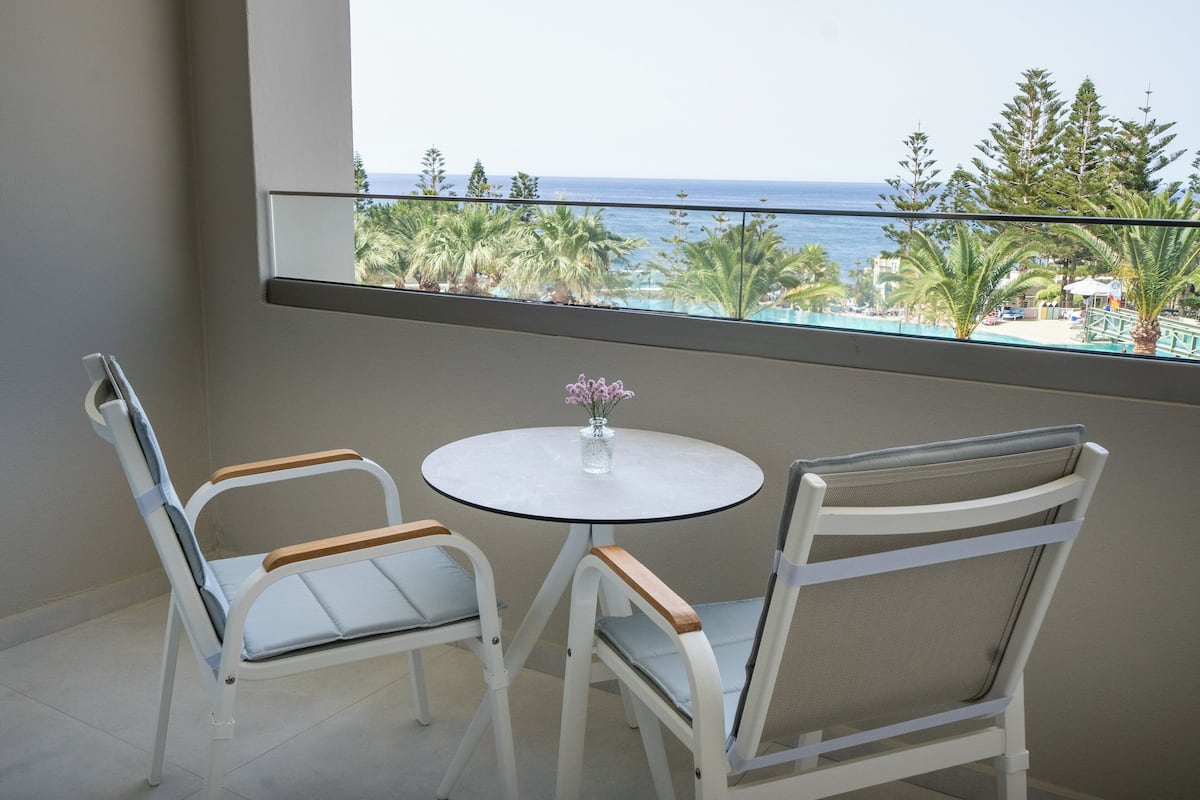 A balcony with a view of the sea, two chairs, and a small table with a vase.