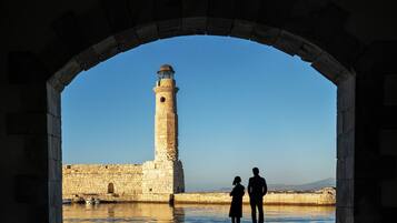 Un arco de piedra enmarca la vista de un faro y una pared de piedra, con una masa de agua al frente.