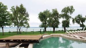 Una piscina con cubierta de madera y sillas de descanso, rodeada de árboles y vistas al agua.