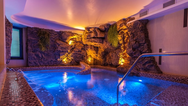 Un jacuzzi con cascada, rodeado de paredes de roca y piso de baldosas.