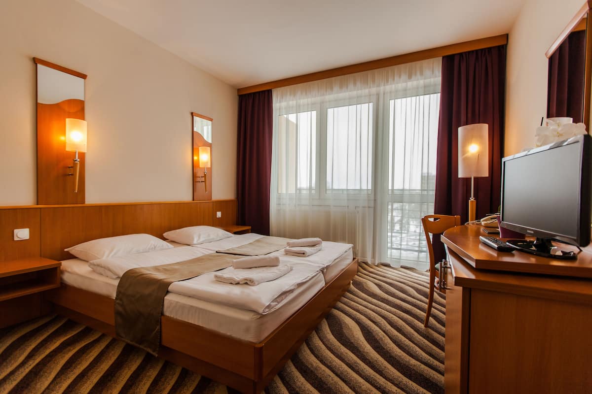 A hotel room with a large bed, a desk with a computer, a mirror, and a window with curtains.