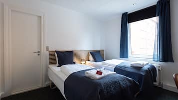 Une chambre d’hôtel avec deux lits, une fenêtre avec des rideaux, un radiateur et une porte.
