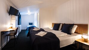 Une chambre d’hôtel comprenant un lit, un bureau, une chaise, un téléviseur fixé au mur et une table de chevet avec une lampe.